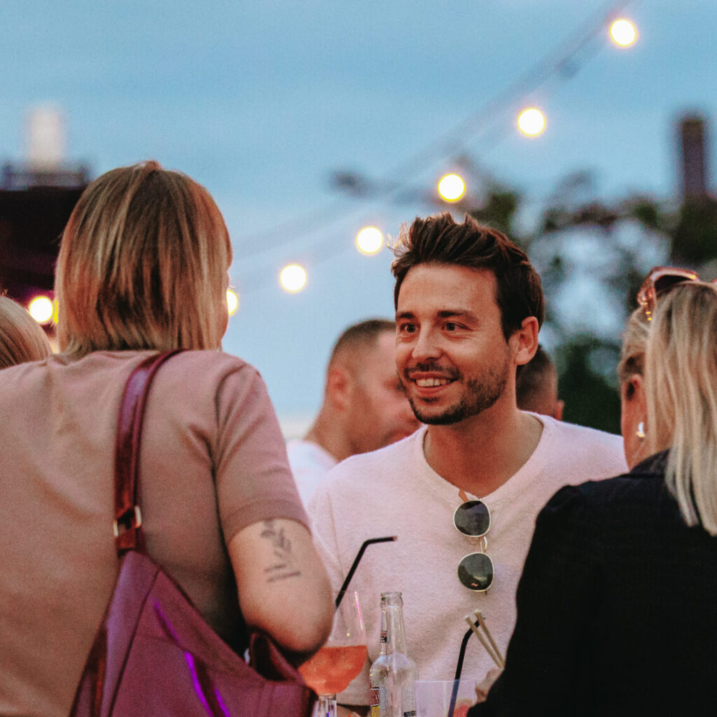 Bezoekers praten onder lichtslingers op Open Air Apero met zomerse sfeer.